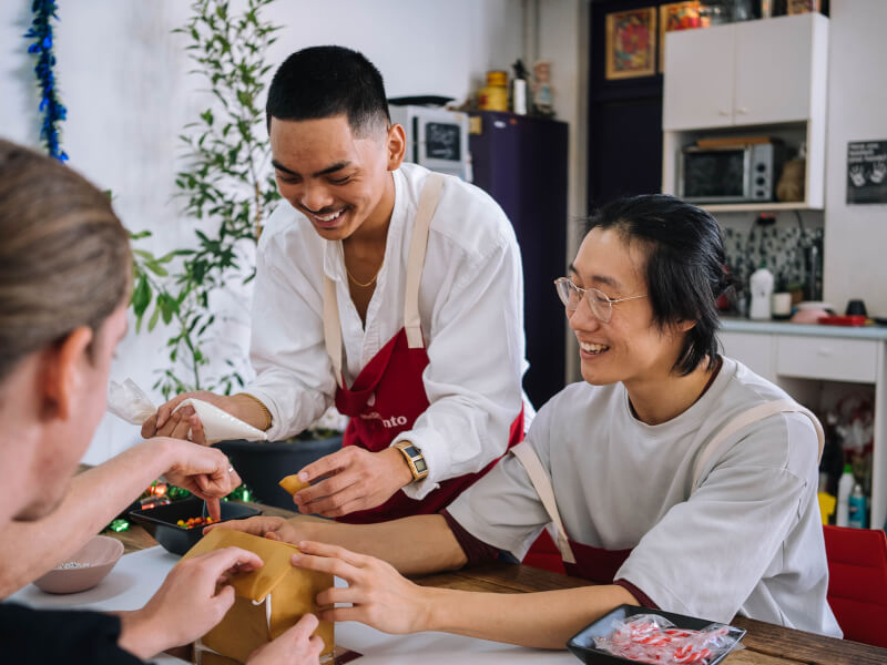 Two men laughing whilst decorating gingerbread house